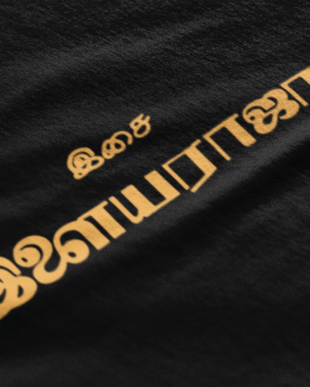 Close-up of black Ilaiyaraaja graphic t-shirt with yellow Tamil script design by METRO ALIEN