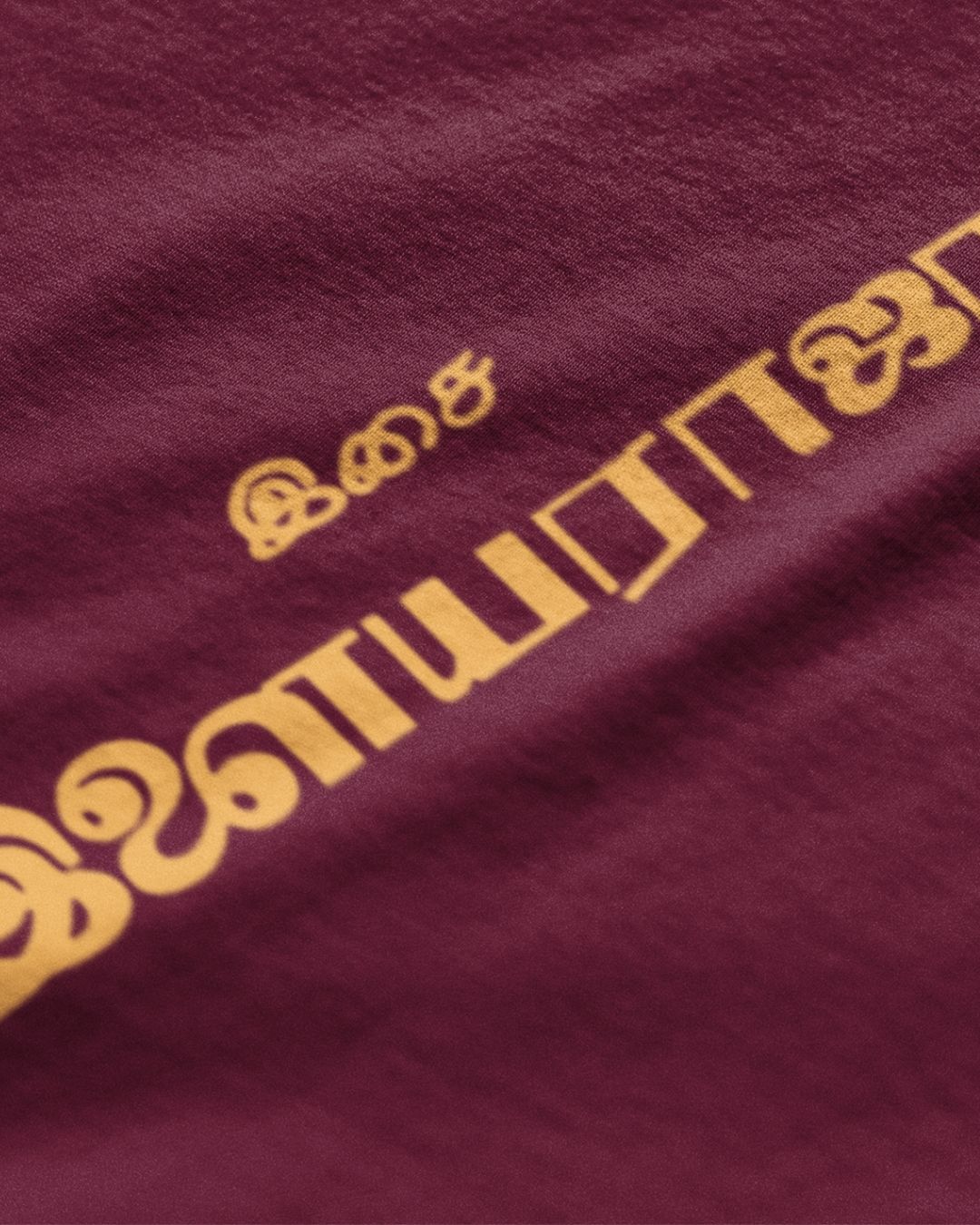 Close-up of maroon Ilaiyaraaja graphic t-shirt with yellow Tamil script print from METRO ALIEN
