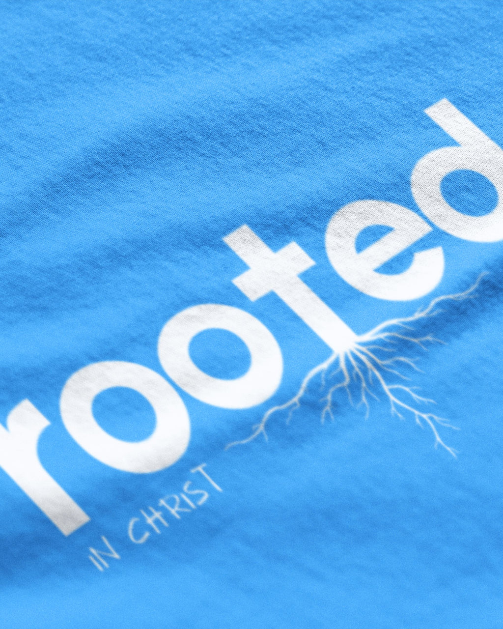 Close-up of blue rooted in Christ t-shirt with white lettering and root design by METRO ALIEN