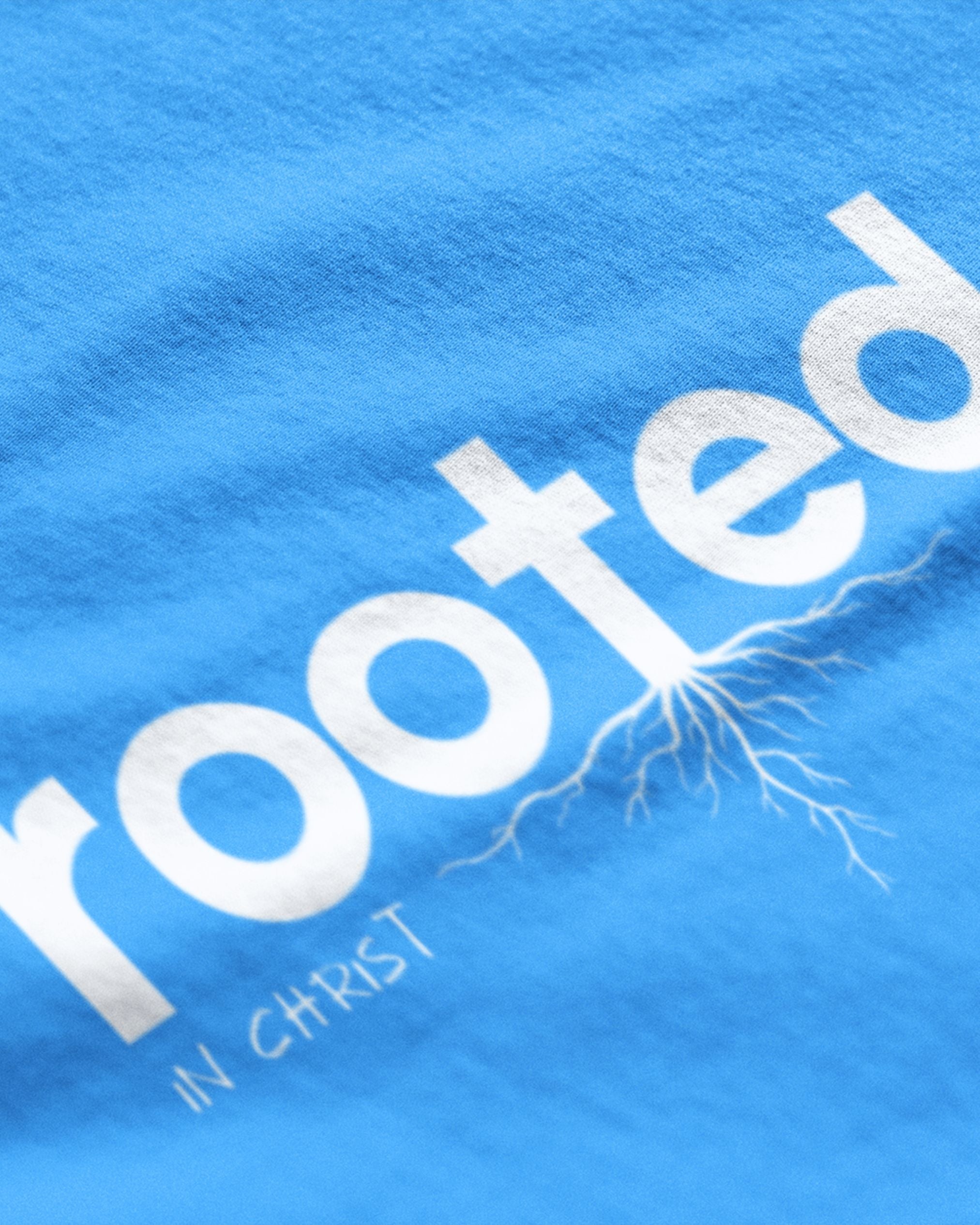 Close-up of blue rooted in Christ t-shirt with white lettering and root design by METRO ALIEN